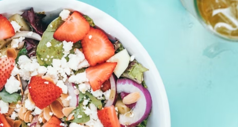 a flatlay salad with fruit and onions and iced tea on a dinner table