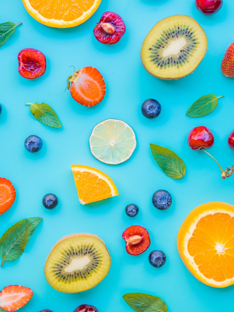 different fruits, kiwi, cherries, orange blubbery strawberry, lemon and basil green leaves isolated on blue